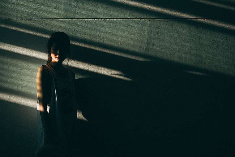 A young woman stands in the shadows.