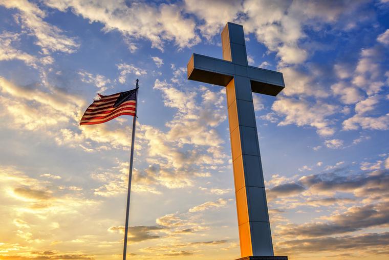 American flag waves next to a cross at sunset.