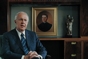Supreme Knight Carl Anderson sits in his office with a picture of Blessed Michael McGivney behind him.