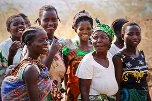 A group of colorfully dressed African women and babies gather at a clean water pump in Malawi.