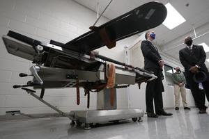 Gov. Ralph Northam, left, stands near a gurney with Greensville Correctional Center warden Larry Edmonds, right, at the Greensville Correctional Center prior to signing a bill abolishing the state's death penalty in Jarratt, Va., Wednesday, March 24, 2021.