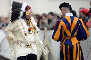 A Native American man wearing traditional regalia walks past a Swiss Guard during Pope Francis’ weekly general audience in St. Peter's Square at the Vatican on April 27, 2016.