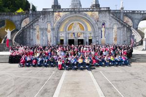 Malades and members of the Order of Malta pose for a picture in front of the Rosary Basilica.