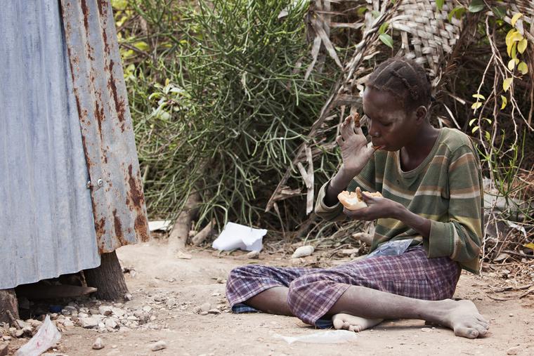 Young Haitian girl sitting on the ground eating peanut butter bread given to her by missionaries.