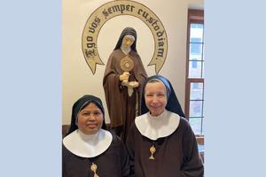 In the Adoration Monastery in Cleveland, Poor Clares Sister Mary Jacinta of the Immaculate Heart of Mary (l) and Sister Mary Joseph of the Most Precious Blood of Jesus stand before a statue of St. Clare, their order's foundress. The Latin phrase stenciled on the wall can be translated as ‘I will always defend you.’