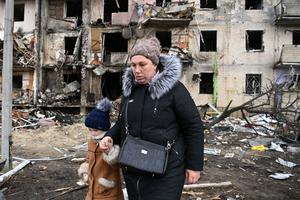 A woman with a child walks in front of a damaged residential building at Koshytsa Street, a suburb of the Ukrainian capital Kyiv, where a Russian military shell allegedly hit, on Feb. 25