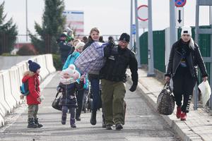 Ukrainian women with children are helped to carry their bags by a Polish border guard as Ukrainian refugees cross the border from Ukraine to Poland at the Korczowa-Krakovets border crossing, in Poland, on Feb. 26, following the Russian invasion of Ukraine.