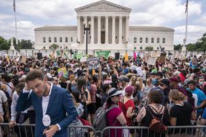 A journalist reports near a crowd of pro-abortion activists in front of the U.S. Supreme Court after the Court announced a ruling in the Dobbs v. Jackson Women's Health Organization case on Friday in Washington, DC.