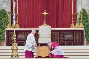 Archbishop Georg Gänswein (right), the longtime personal secretary for Benedict XVI,  kneels to kiss the book of the Gospels atop the coffin of the pope emeritus on Jan. 5, 2023, in St. Peter's Square