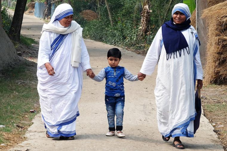 Two Missionaries of Charity walk with a child in Chunakhali, West Bengal, India