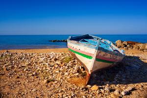 A broken migrant boat sits stranded on a beach. 
