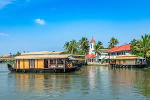 Old colonial Saint Thomas Catholic Church on the coast of Pamba river, with palms and anchored living houseboats in Alleppey, Kerala. 