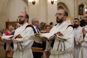 The entrance into the Franciscan church in Aleppo, Syria, of the twins George and Johnny Jallouf, friars of the Custody of the Holy Land, who were ordained priests on July 6, 2024. The two ordinands are wearing the priestly vestments with which they were clothed during the ordination rite. They were 15 when the war in Syria broke out. Their vocation was born and grew amid the Battle of Aleppo. “I tried to attend Mass every day,” George recounted. “I was afraid, but I kept repeating to myself ‘I fear nothing because you are with me.’ This phrase guided me, reassured me, gave me peace.”