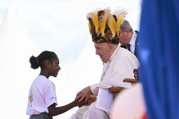 Pope Francis wears a traditional head dress as he greets a young girl in Vanimo, Papua New Guinea, Sept. 8.
