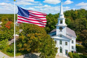 A church and U.S. flag stand over the historic Town Common in Carlisle, Massachusetts.