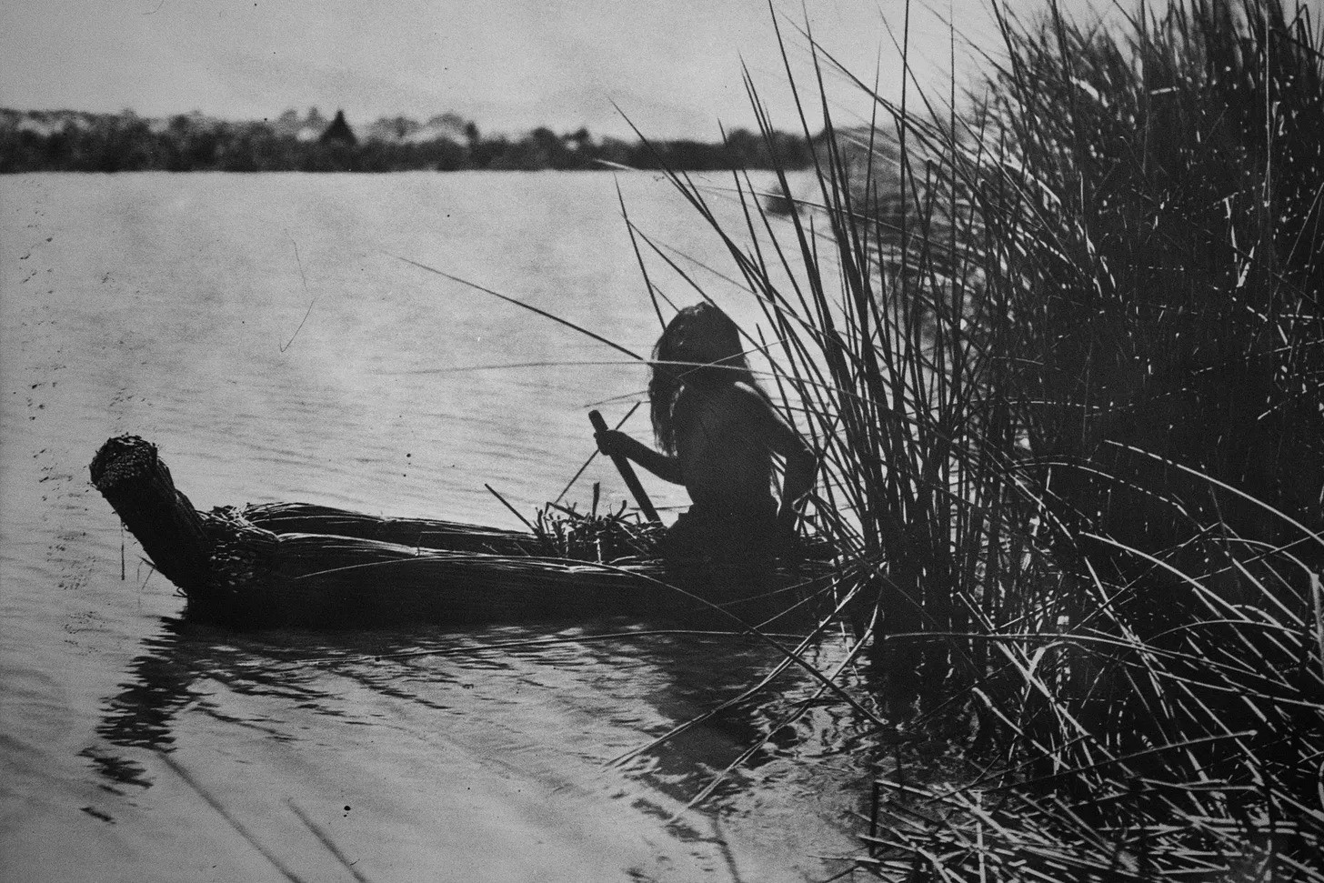 A historical photo depicting a Native Californian paddling a tule reed canoe