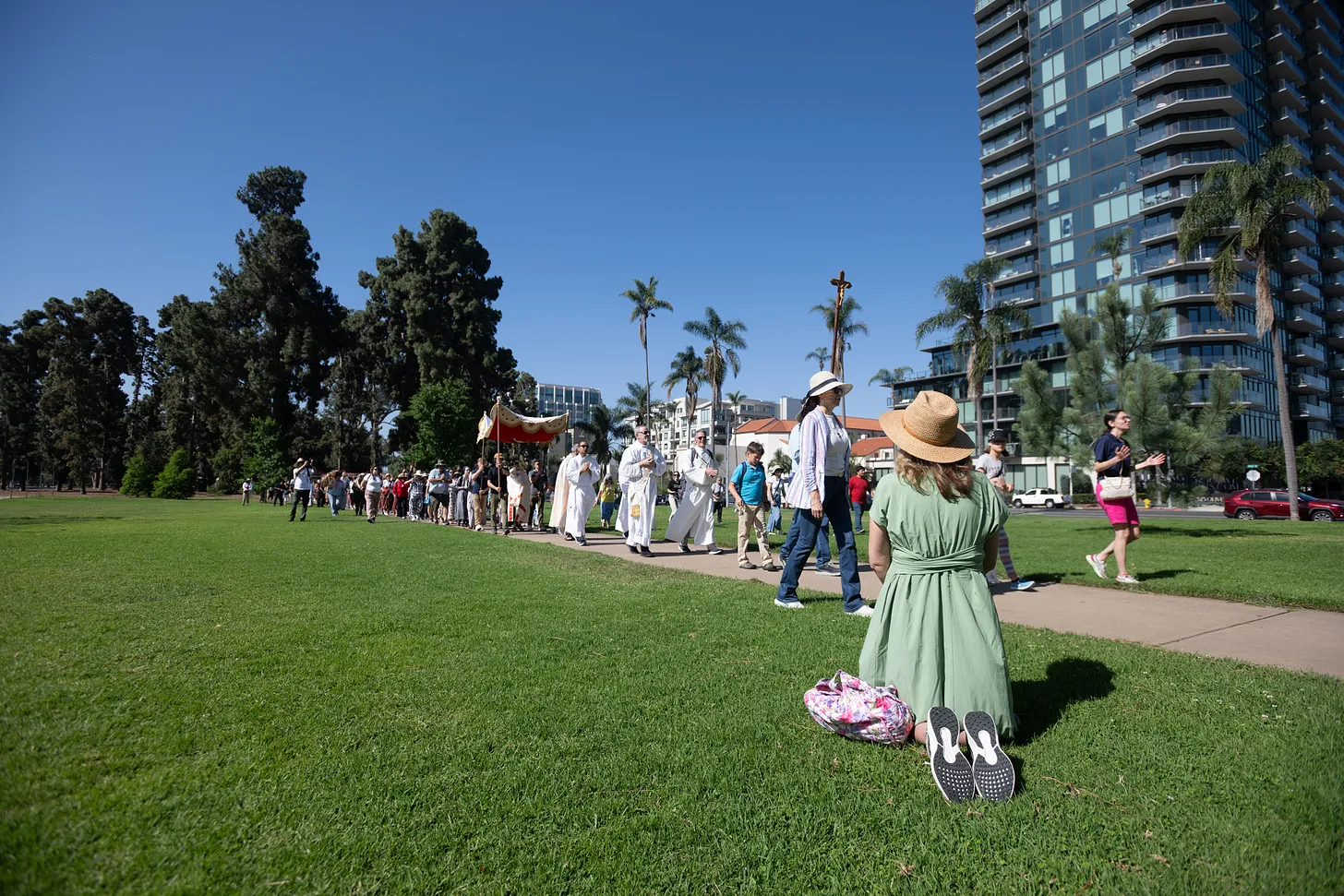 A woman kneels in reverence as pilgrims from the National Eucharistic Pilgrimage process through Balboa Park.