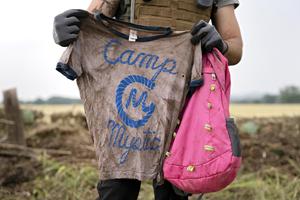 A volunteer searches along the Guadalupe River near Ingram, Texas, on July 6, holding a Camp Mystic T-shirt and backpack. More than 160 people — including dozens of children from the flood-destroyed Christian camp — are still missing following the historic flash floods that swept through Central Texas over the Fourth of July weekend.