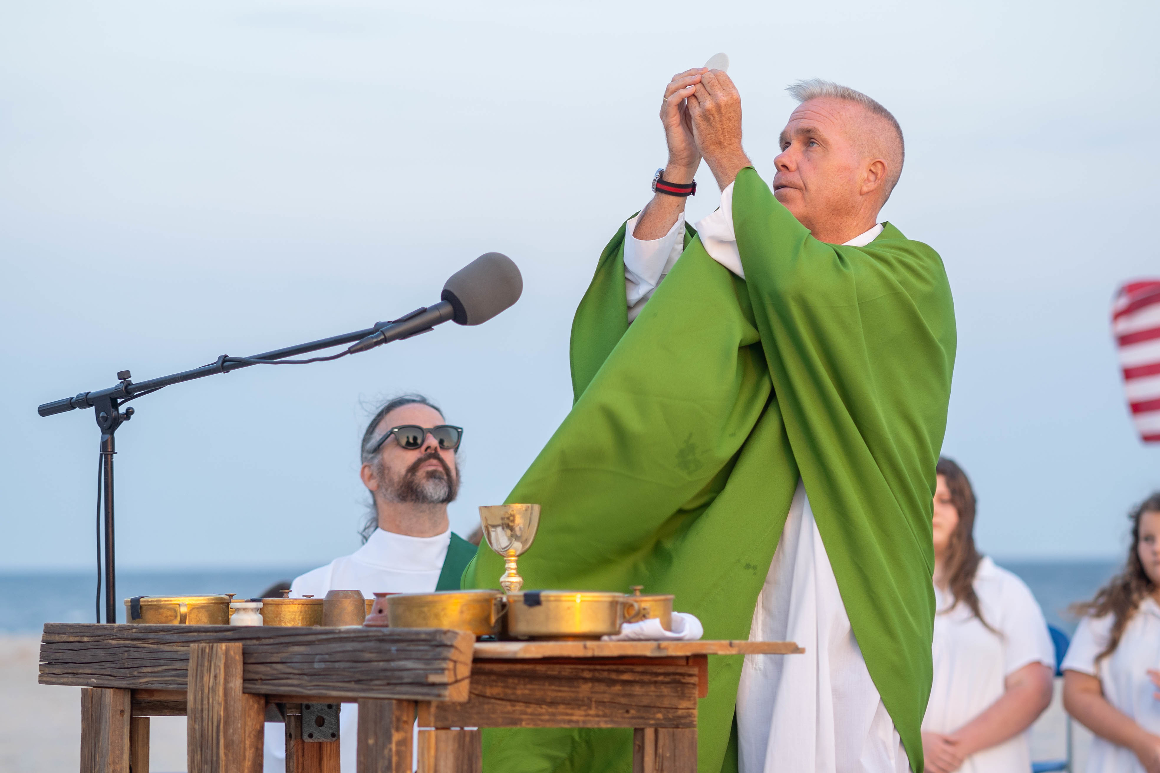 Padre Brian Barr eleva a Eucaristia durante Missa na praia
