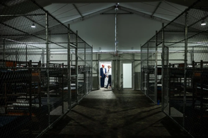 Rows of bunk beds line the interior of the so-called ‘Alligator Alcatraz’ detention facility in the Florida Everglades, a repurposed training center now designated for holding immigrants. President Donald Trump appears in the background during a July 1, 2025, visit to the site.