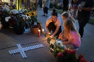 Jen Labanowski, her daughter Lucy (r), and her daughter's friend Cece Degnan (c), light candles on Thursday at a memorial for victims of Wednesday’s shooting in front of Annunciation Catholic Church in Minneapolis.