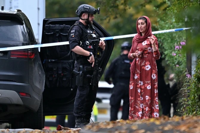 An armed police officer talks to a member of the local community outside Heaton Park Hebrew Congregation synagogue in Crumpsall, north Manchester, England, on Thursday, Oct. 2, 2025.