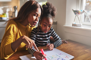Mother helps daughter with writing. 