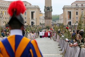 Swiss Guards and faithful pilgrims holding olive branches line the processional route in St. Peter’s Square for Palm Sunday celebrations, April 13, 2025. The ancient Vatican obelisk stands at the center of the square as clergy process toward the basilica.