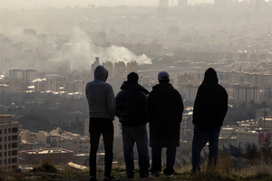 Men watch from a hillside as a plume of smoke rises after an explosion on March 2, 2026, in Tehran, Iran. The United States and Israel continued their joint attacks that erupted on Feb. 28. 