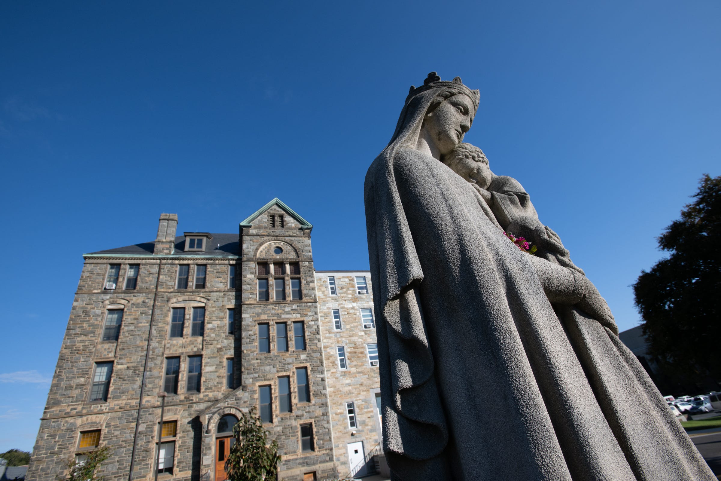 The Blessed Mother holds the infant Jesus with the campus of CUA behind her. 