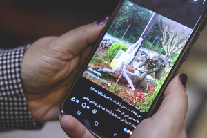 A woman checks a social-media post on her mobile phone featuring an image that appears to show an Israeli soldier hitting a statue of Jesus Christ in the southern Lebanese Christian village of Debel, in Beirut, on April 20, 2026. The photo, which the military determined was authentic after it spread online, shows an Israeli soldier using a sledgehammer to strike the head of a statue of a crucified Jesus. 