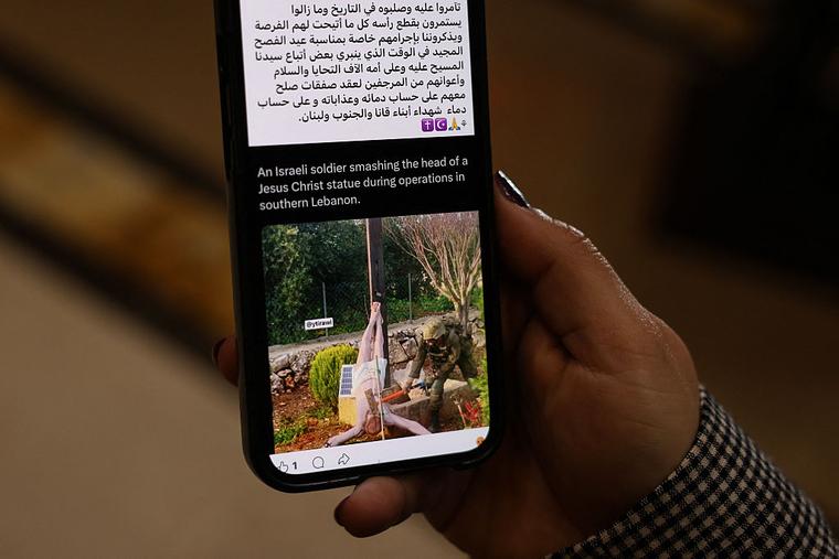 A woman checks a social media post on her mobile phone featuring an image that appears to show an Israeli soldier hitting a statue of Jesus Christ in the southern Lebanese Christian village of Debl, in Beirut on April 20, 2026.