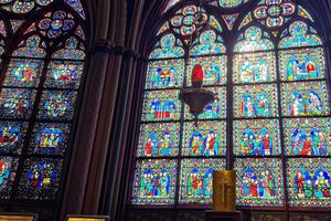 A red sanctuary lamp hangs before a Gothic stained-glass window inside Notre-Dame Cathedral in Paris.