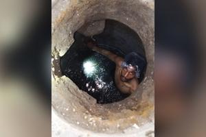 Akash Masih wears a plastic bag over his head to prevent dark sewage sludge from getting on his hair while cleaning a manhole in Johar Town, Lahore, on May 9, 2026. 
