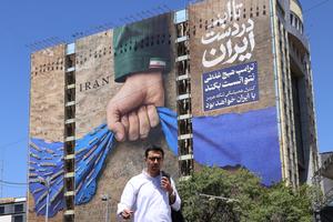A man crosses a street past a billboard on the facade of a building depicting the Strait of Hormuz with a caption in Persian reading "Forever in Iran's Hand" in Tehran’s Vanak Square on May 25.