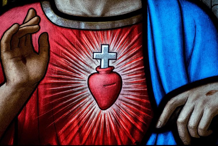 Light shines through a stained-glass image of the Sacred Heart of Jesus.