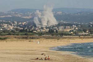 A photograph taken from the southern city of Tyre, Lebanon shows people sunbathing on the beach as smoke rises from the site of an Israeli airstrike in the village of Deir Qanoun Ras al-Ain on June 8, 2026. 