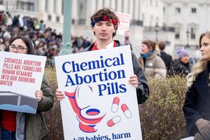 A supporter of the Clean Water for All Life Act holds a sign about the environmental impact of chemical abortion pills on March 18, 2026.